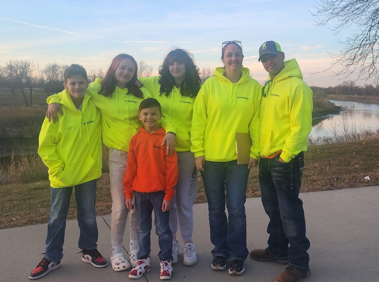 The My Tree Guy LLC family team in company hoodies by the river